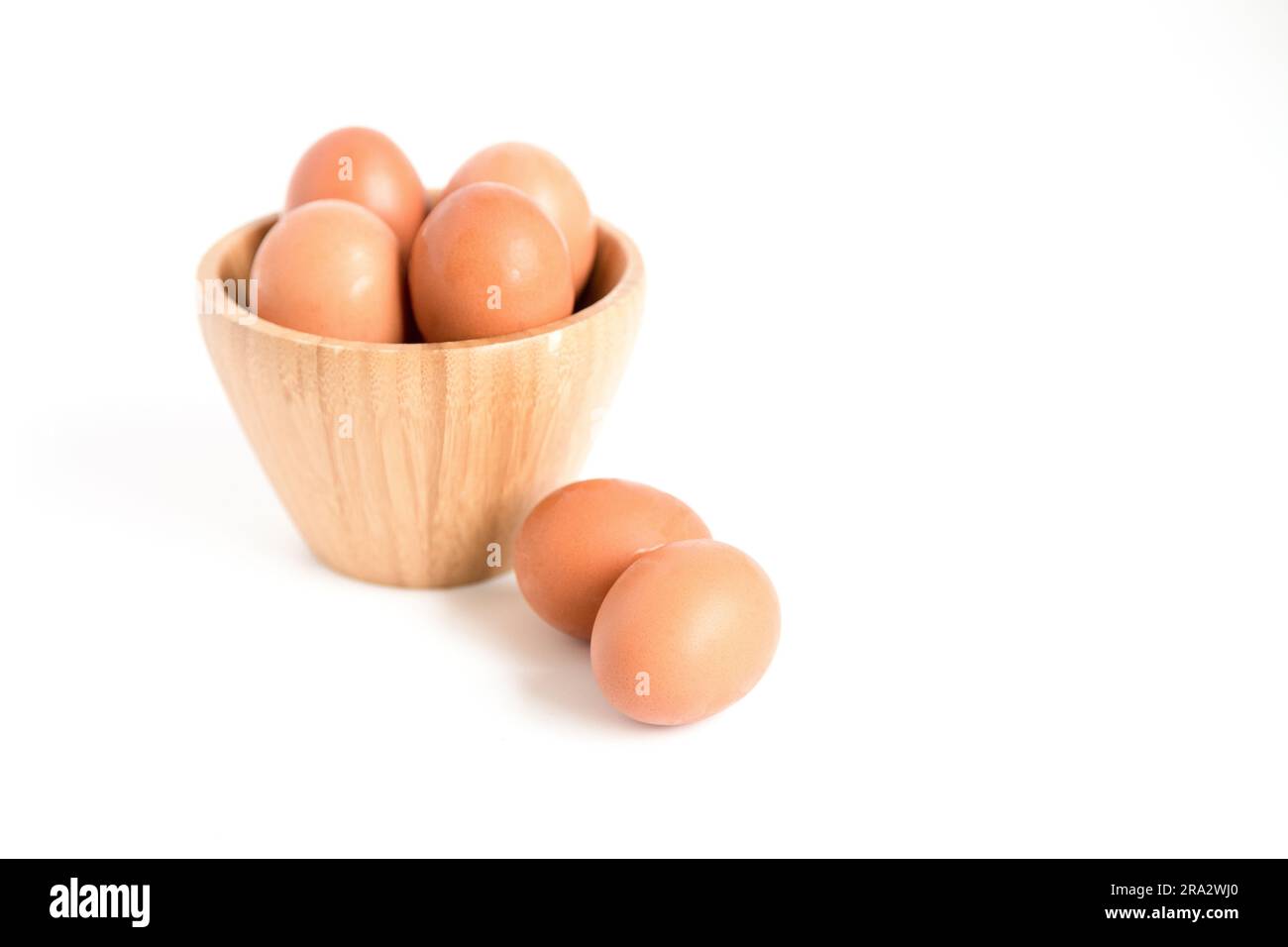 Several fresh chicken eggs placed in and out of a bamboo container on a white background. Copy space. Stock Photo