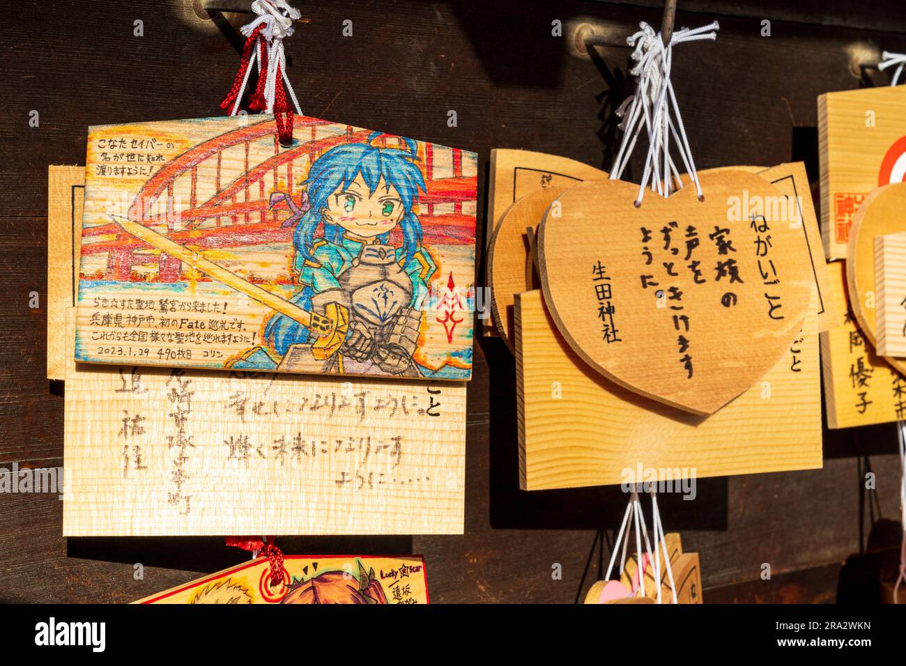 Japanese Shinto ema hanging on wooden board. Ema are wishing, pray tablets. One features an anime character with inscription. Ikuta shrine, Kobe. Stock Photo