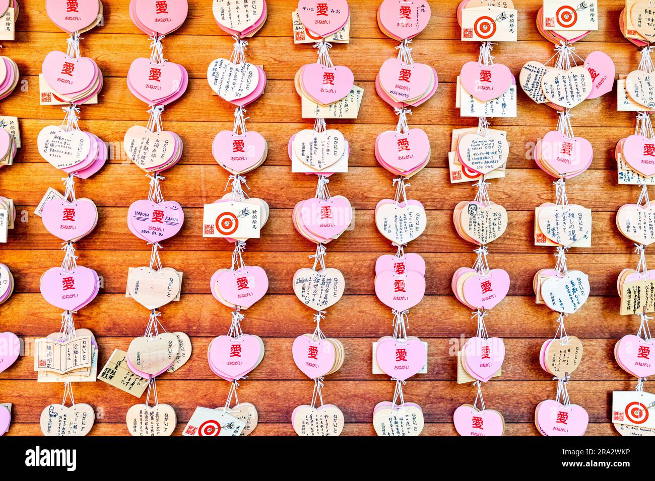 Rows of Japanese Shinto ema hanging on wooden board. Pink heart shaped wooden wishing plaques mixed with traditional shaped ones at Ikuta Shrine, Kobe Stock Photo