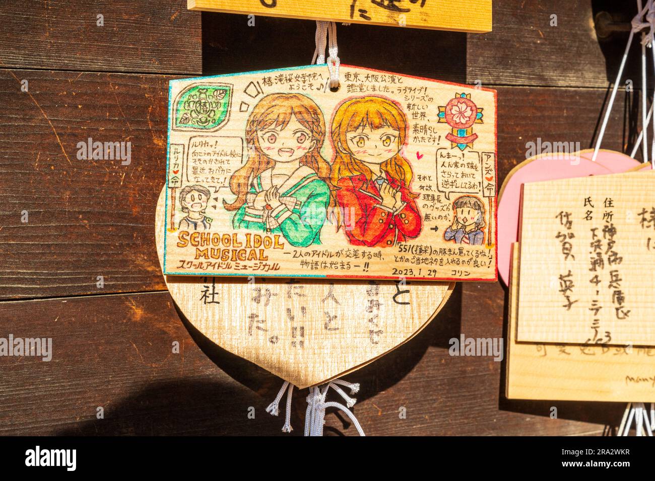 Japanese Shinto ema hanging on wooden board. Ema are wishing, pray tablets. One features two anime schoolgirls with inscription. Ikuta shrine, Kobe. Stock Photo