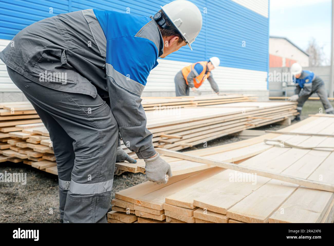 Workers in hard hats and overalls stack wooden boards outside on street