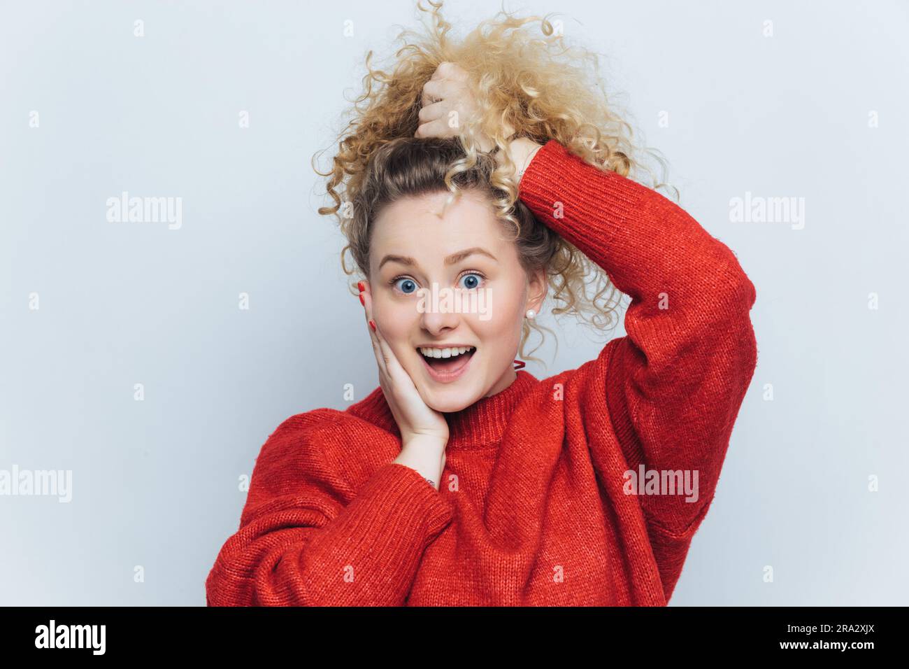 Curly-haired girl, wide-eyed and amazed, mouth open in excitement, models against white background. Awe of her success. Stock Photo