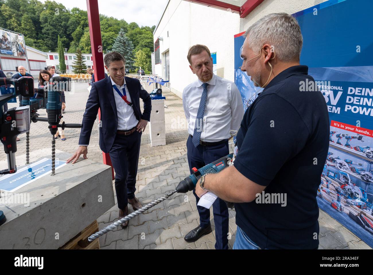 Sebnitz, Germany. 30th June, 2023. Martin Thiel (r), Head of Quality at Bosch Power Tools GmbH, gives a tip to Michael Kretschmer (CDU), Prime Minister of Saxony, who holds a cordless hammer drill in his hands, while Christoph Kilian (l), Managing Director of Bosch Power Tools GmbH, also listens. Bosch Power Tools GmbH in Sebnitz, Saxony, had reached a special anniversary to mark 75 million power tools built. Credit: Daniel Schäfer/dpa/Alamy Live News Stock Photo