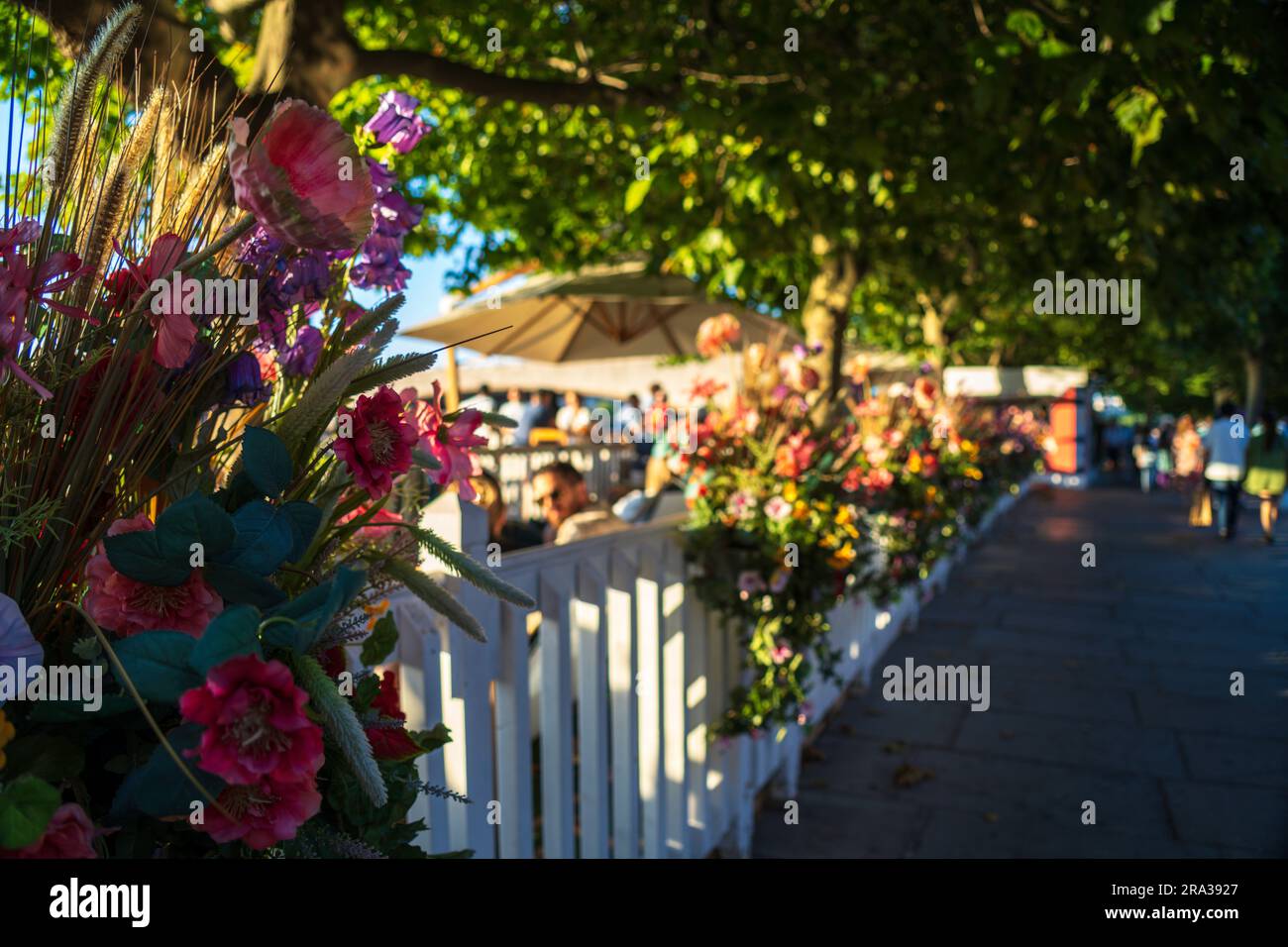 Unrecognizable people talking while enjoying food and drinks at a restaurant, bar on the Thames River embankment in London. Flowers in the foreground Stock Photo