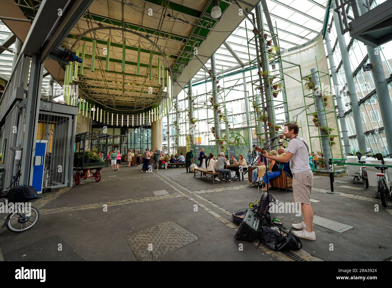 Borough Market, London's oldest food market, a musician performs at the historic food hall as people shop, eat fresh meals and talk to friends, family Stock Photo
