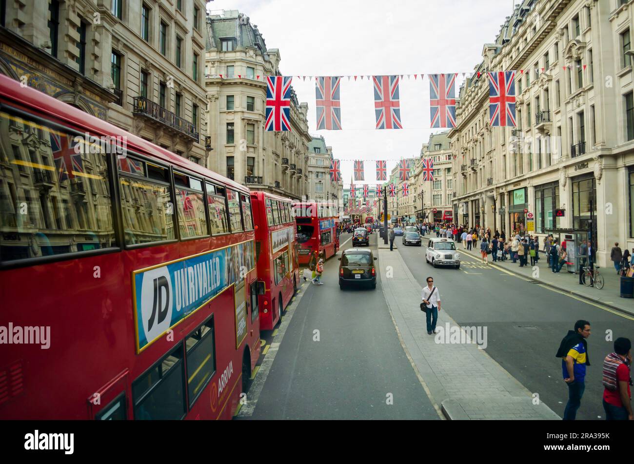UK flags decorate a busy London street as iconic black cabs and red double-decker buses pass. UK flags decorate the streets for coronations, jubilees Stock Photo