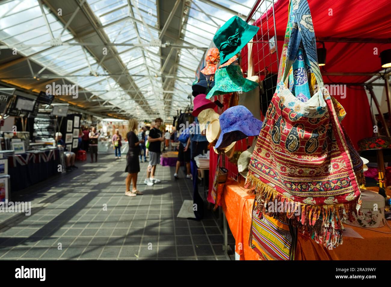 People shopping at Greenwich Market in downtown Greenwich, London. Bags, hats and other goods hang from the retail stalls of this popular city market. Stock Photo