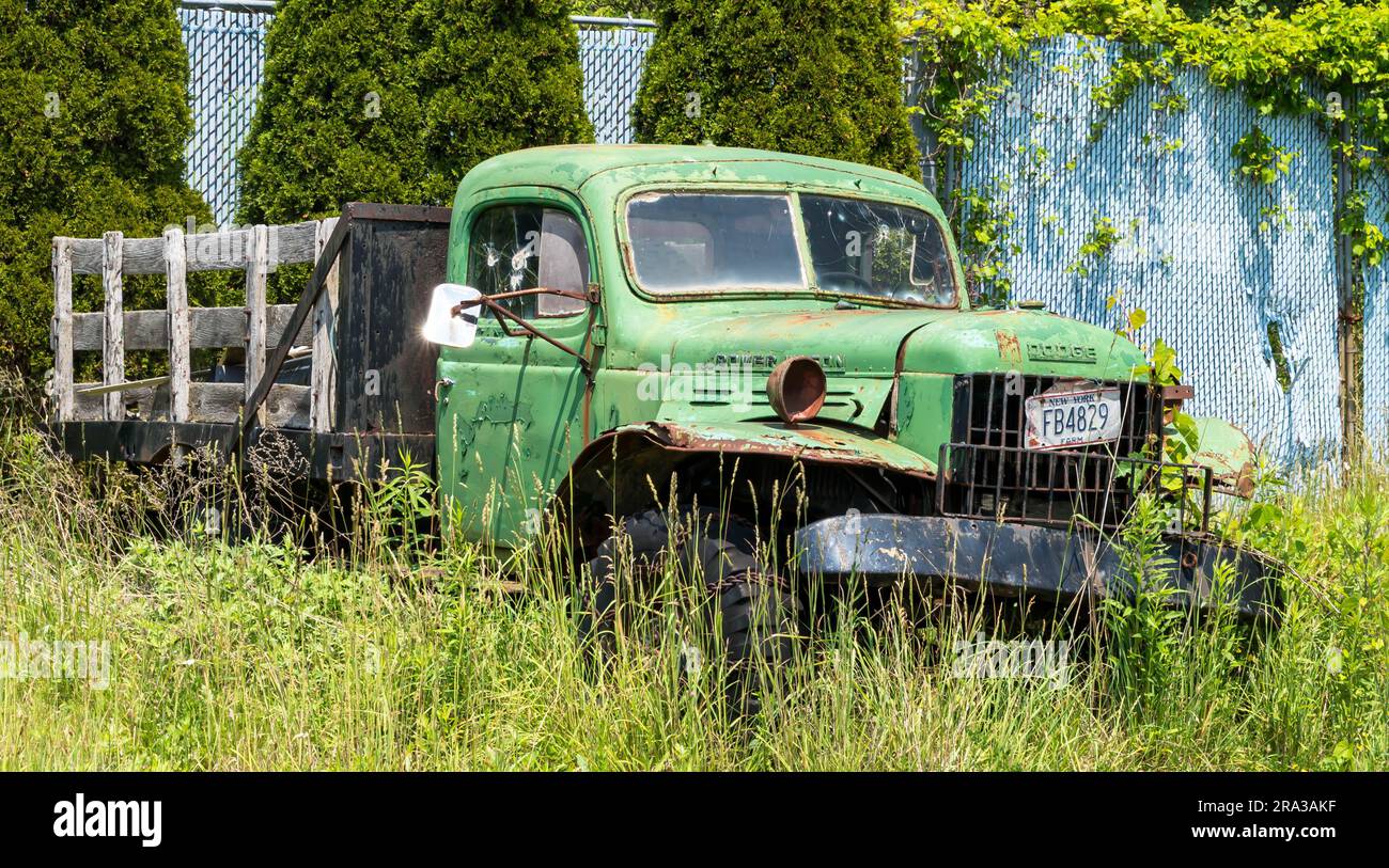 An old, dilapidated green Dodge truck parked in the grass in front of a junk yard in Frewsburg, New York, USA Stock Photo
