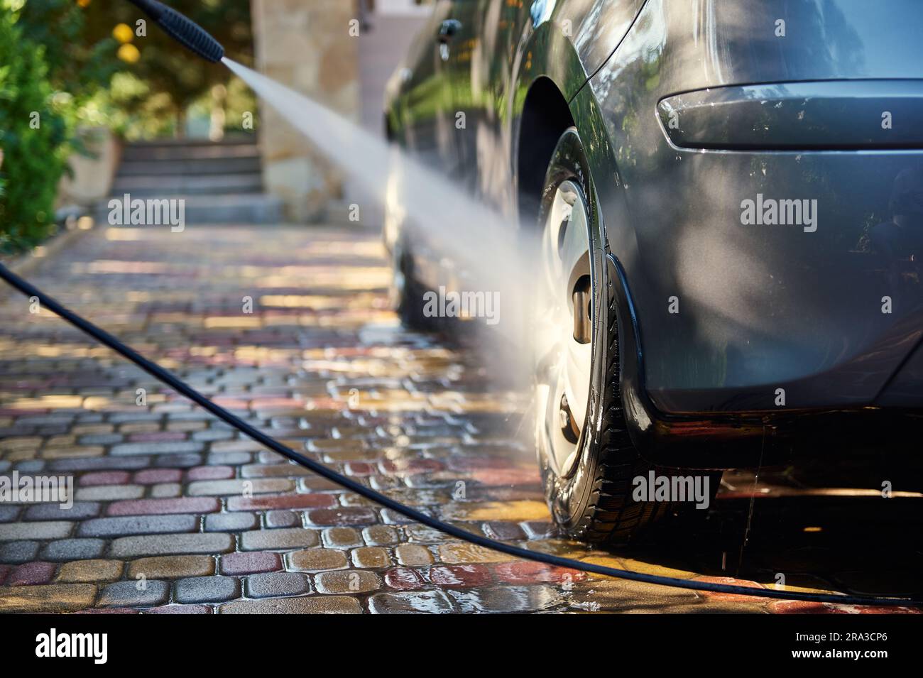 Closeup of car washing process. Unknown man directs a hose with jet of water at the rear wheel