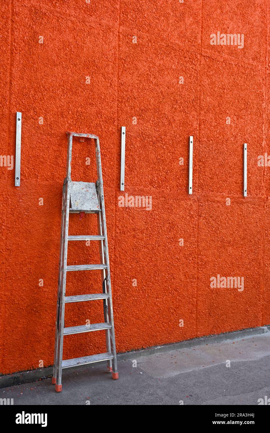 Step ladder resting against bright orange wall Stock Photo
