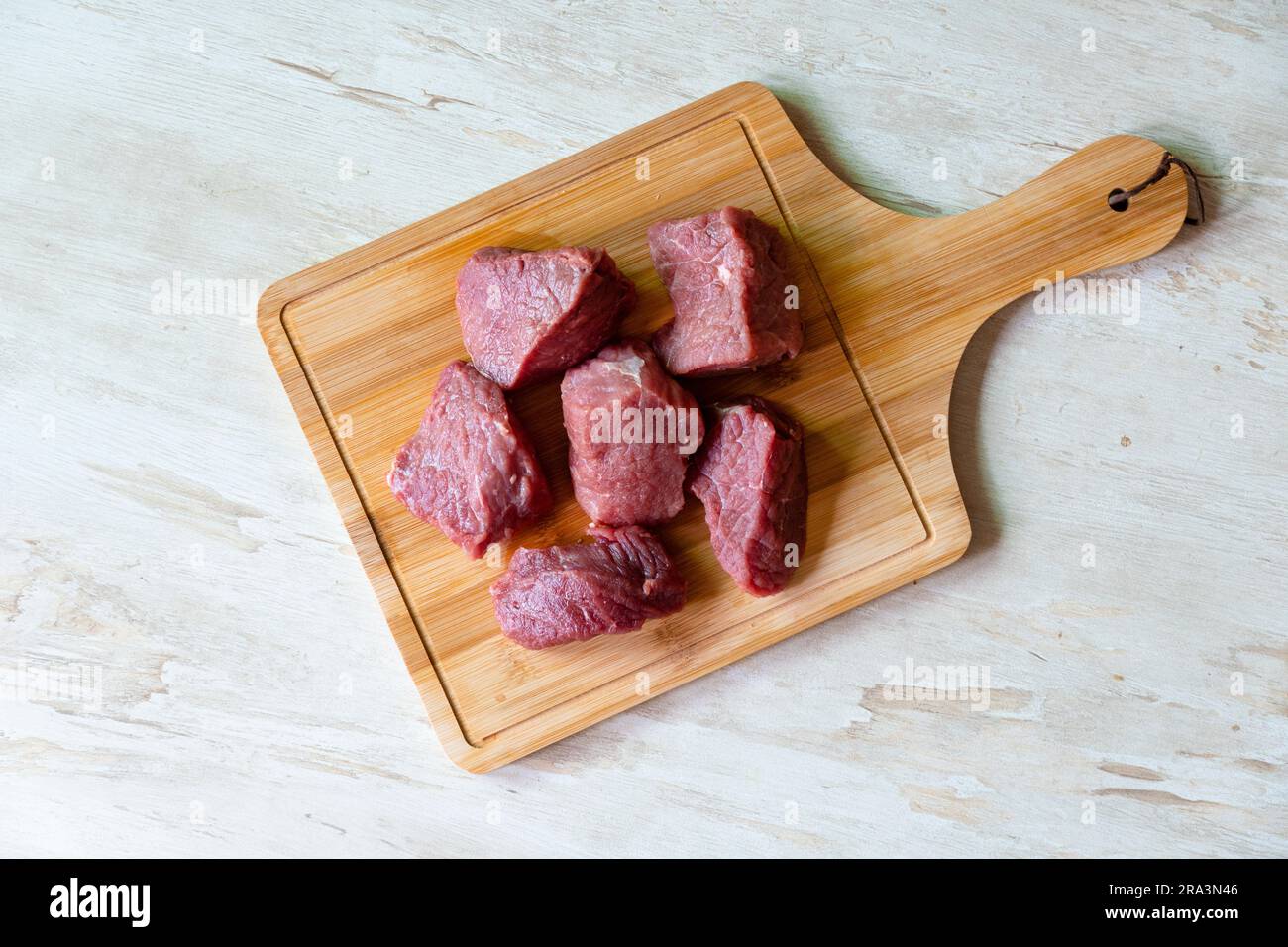https://c8.alamy.com/comp/2RA3N46/raw-beef-meat-on-wooden-cutting-board-for-cooking-stew-or-other-meat-dish-on-white-background-top-view-2RA3N46.jpg