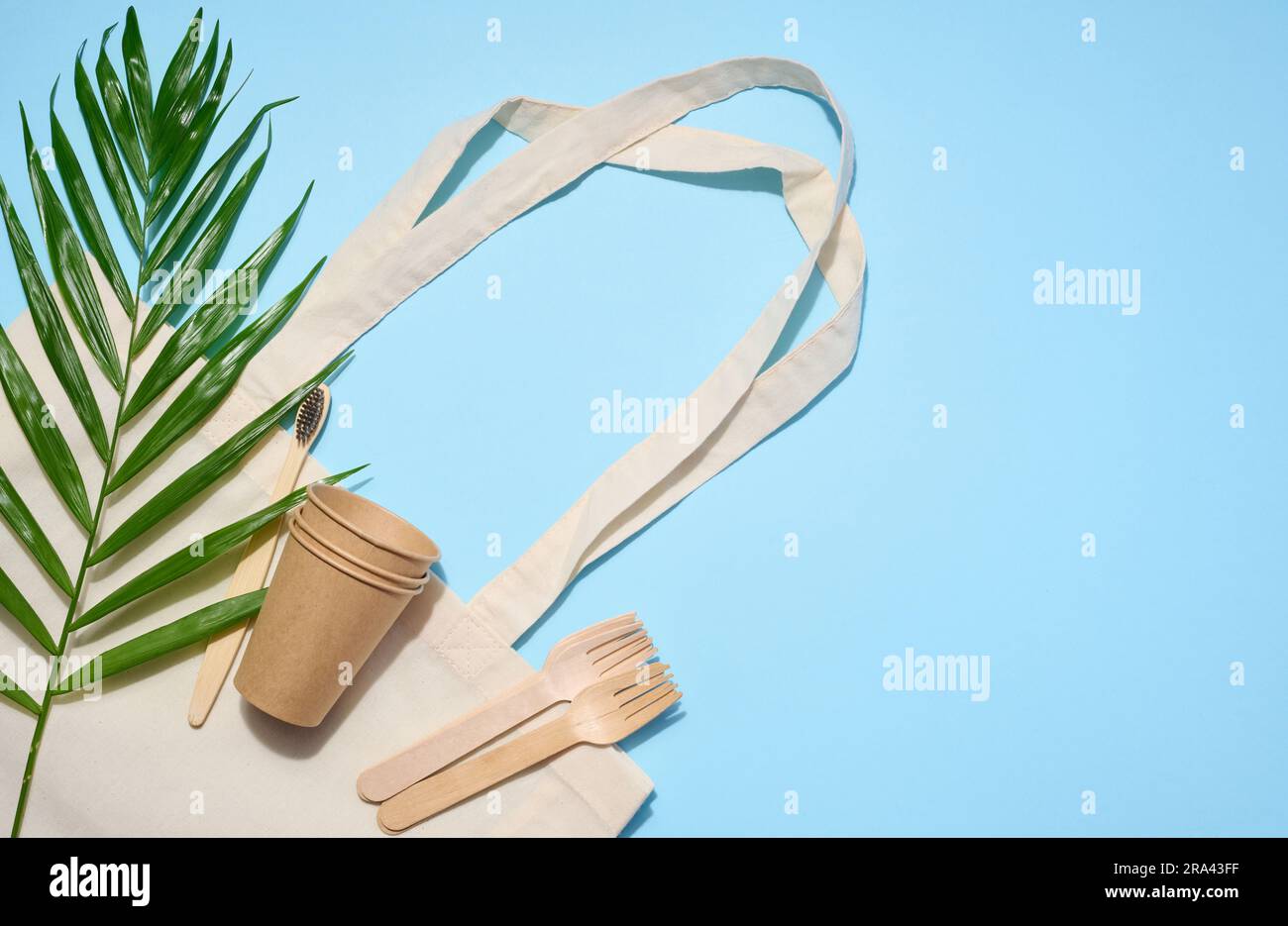 White cotton bag, wooden forks and cups on a blue background. Waste