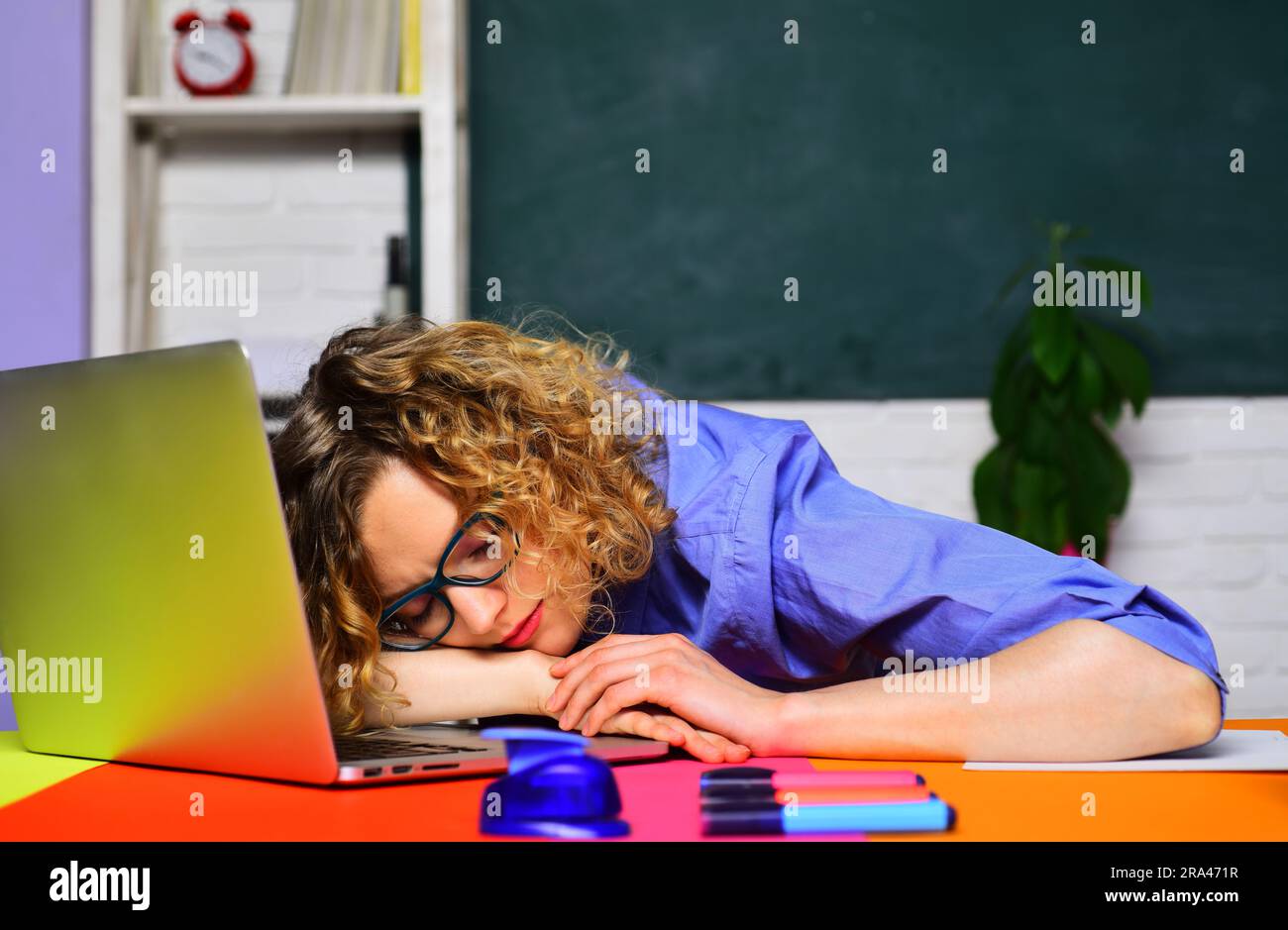 Tired overworked female teacher sleeping on desk in classroom. Back to school. Knowledge day. Student preparing for university exam. Learning and Stock Photo