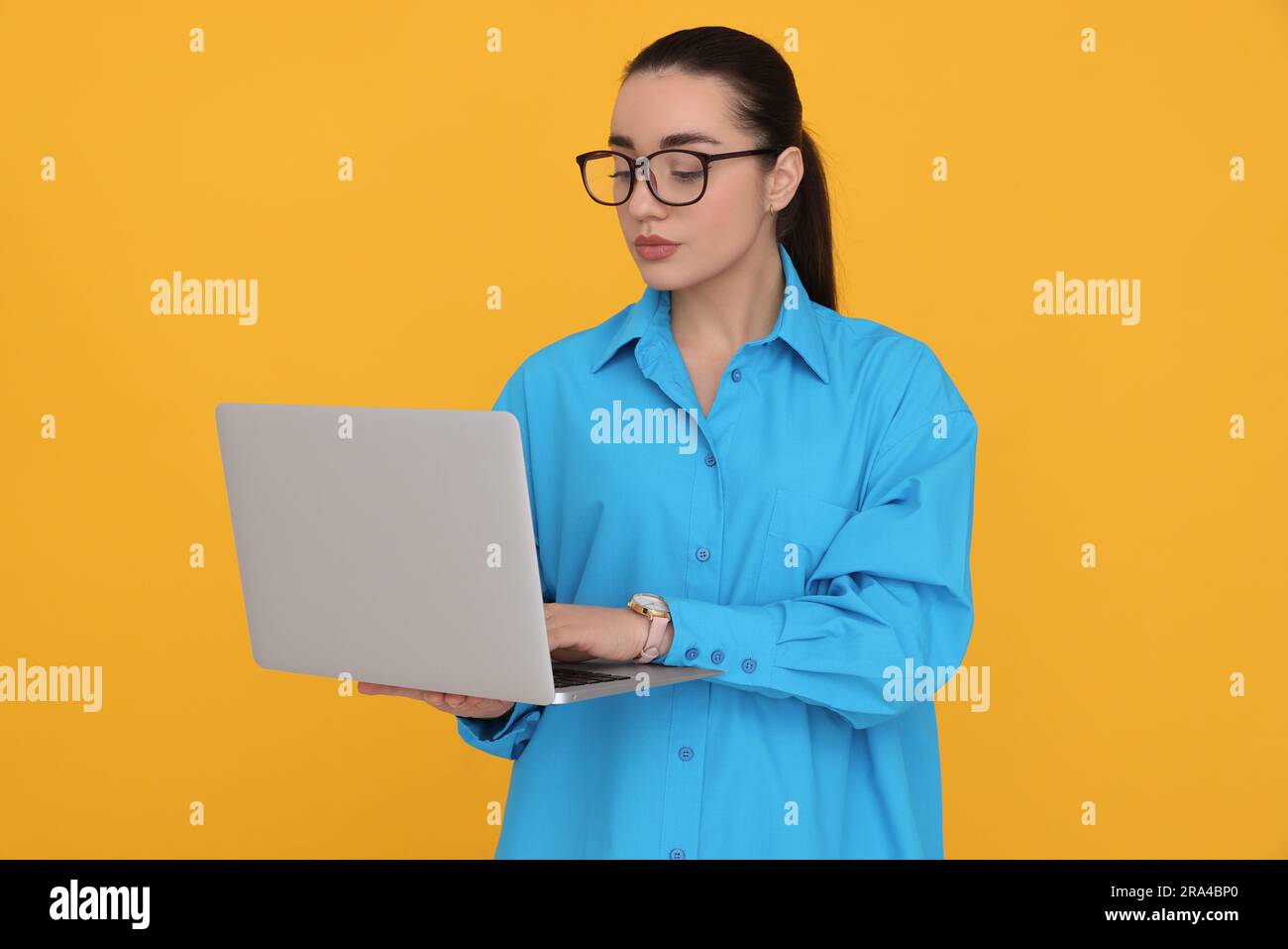 Young female intern with laptop on yellow background Stock Photo