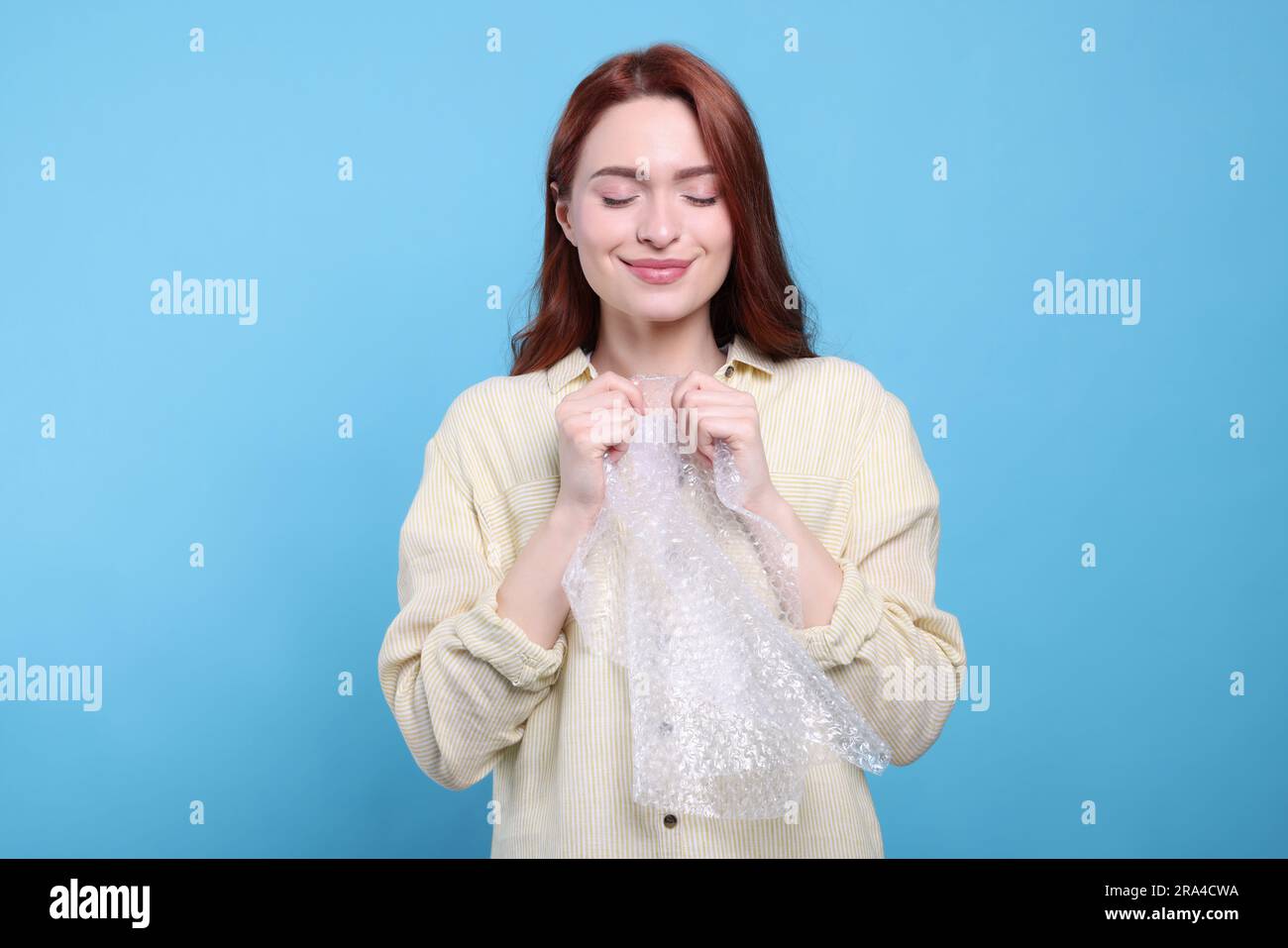 Woman popping bubble wrap on turquoise background. Stress relief Stock
