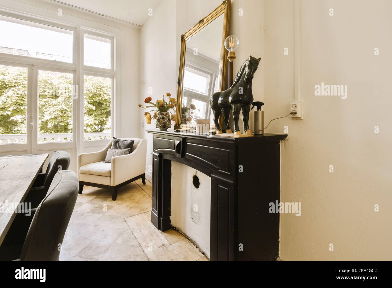 a living room with a table, chairs and a mirror on the wall next to it is a black horse statue Stock Photo