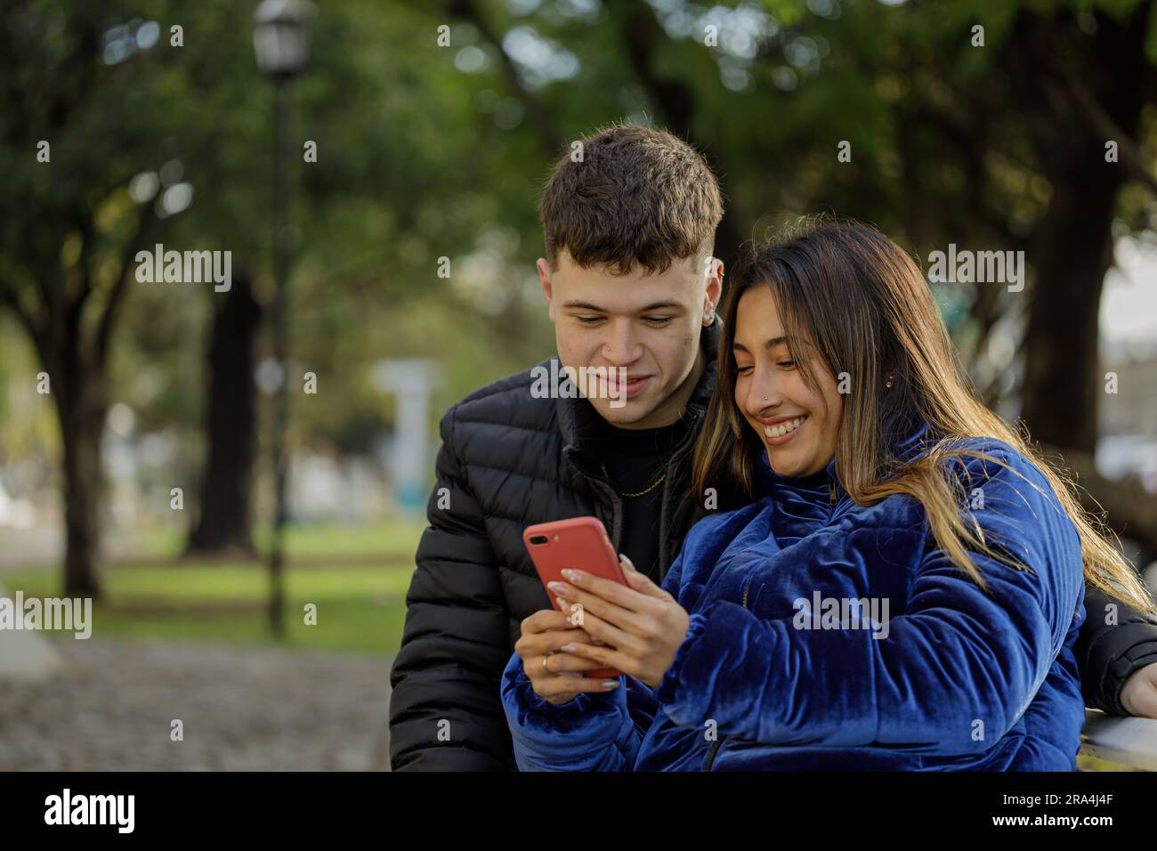 Latina girl and Caucasian boy sitting on a bench in a public park. Stock Photo