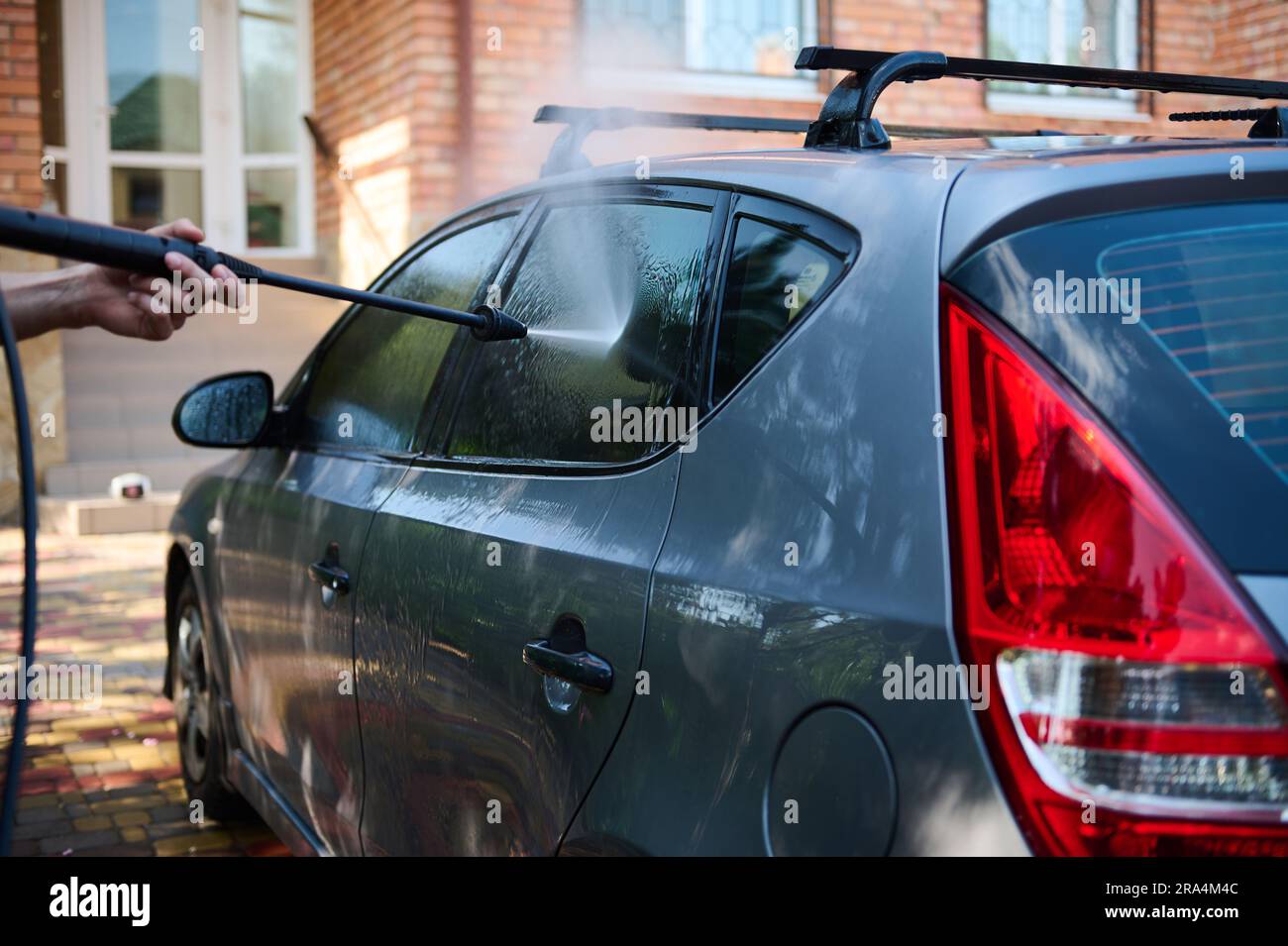 Closeup man manually washing car outdoors using a high pressure washer