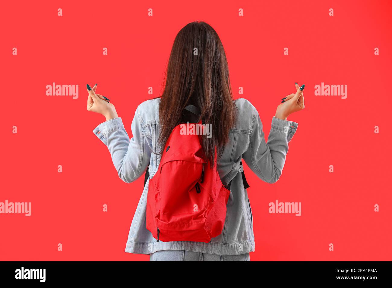 Female student with backpack making heart shape on red background, back view Stock Photo