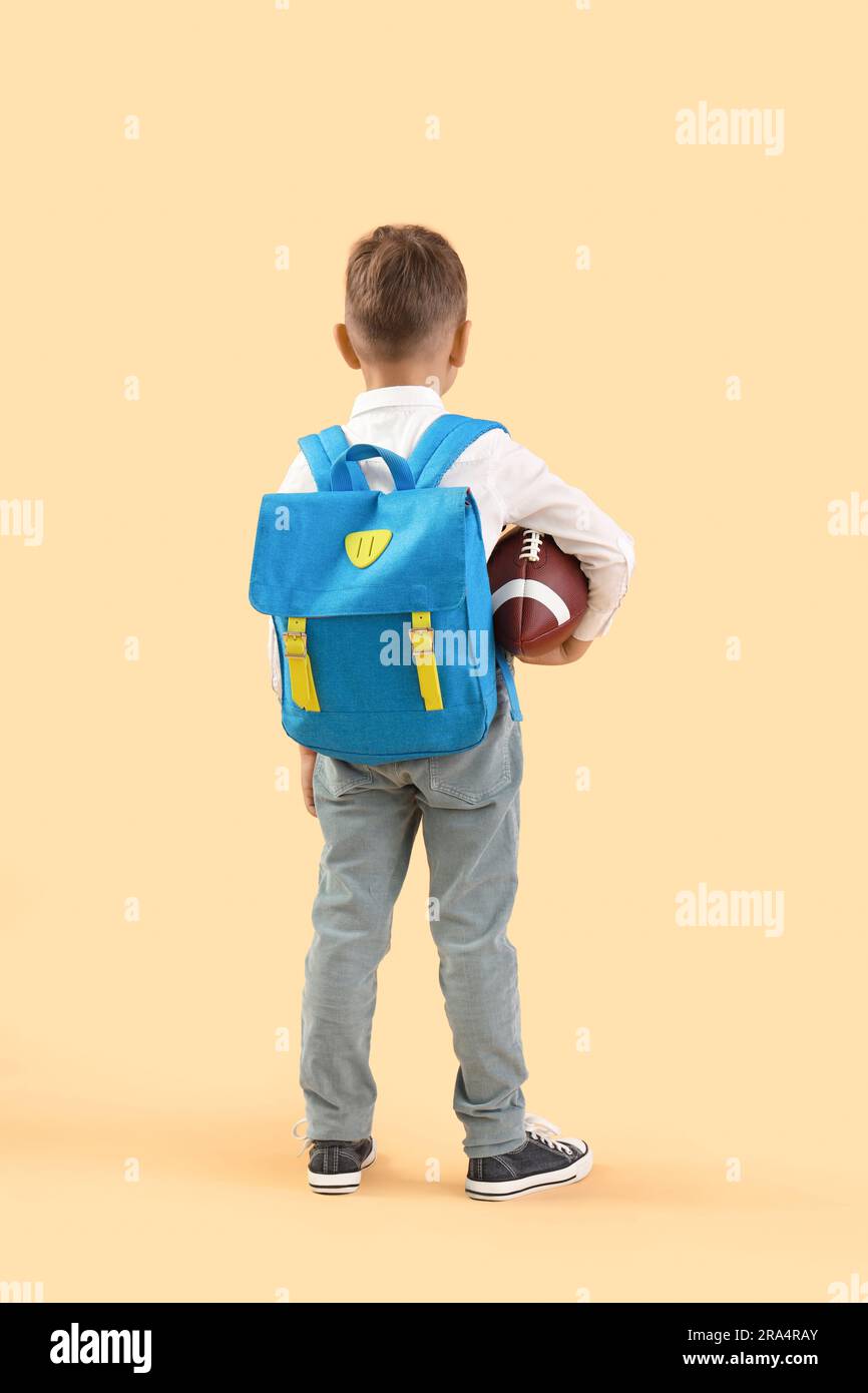 Little schoolboy with blue backpack and rugby ball on orange background ...