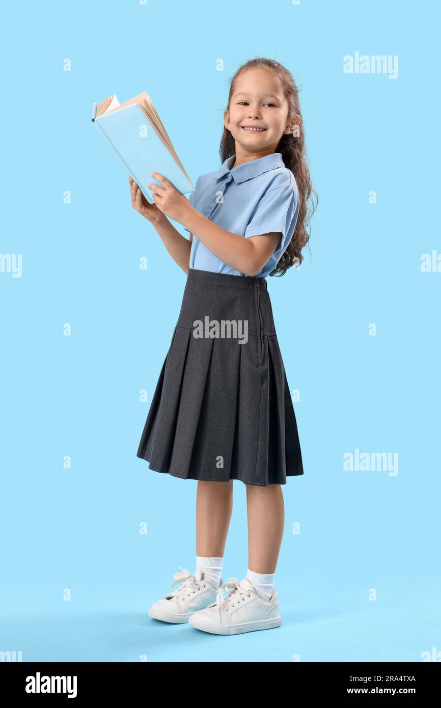 Little schoolgirl with book on light blue background Stock Photo - Alamy