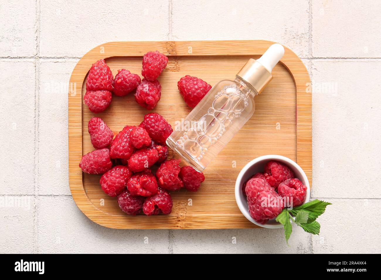 Wooden board with bottle of cosmetic raspberry oil on white tile ...