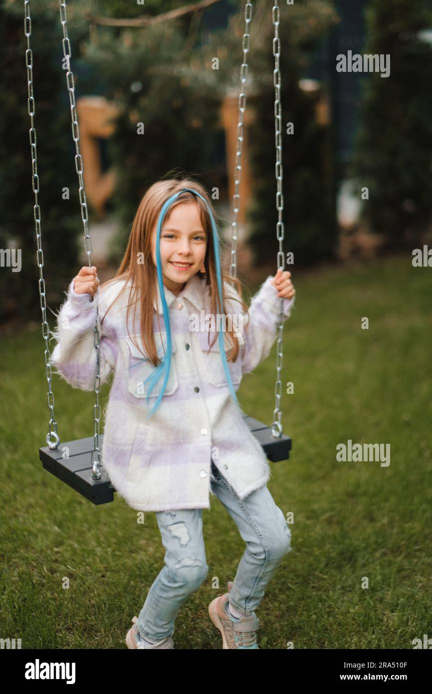 A beautiful girl with long hair in a jacket rides on a swing in the ...