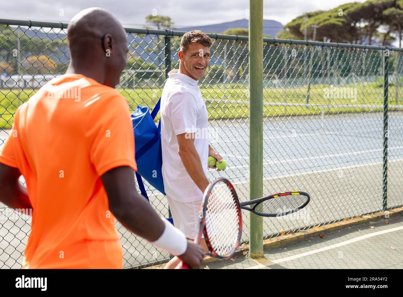 Happy diverse male tennis players with sports bag and rackets talking ...