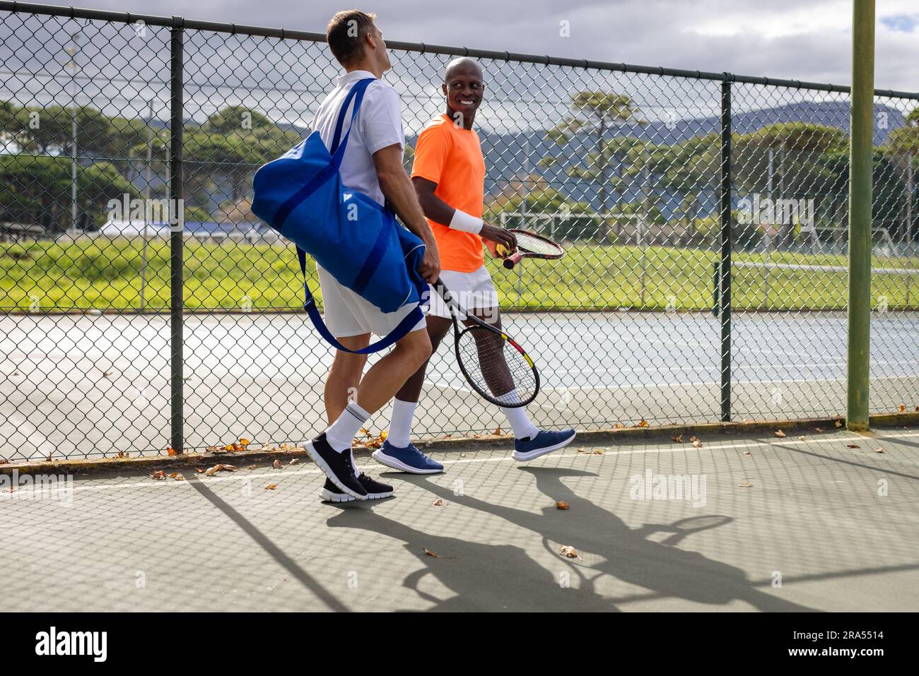 Happy diverse male tennis players with sports bag and rackets talking ...