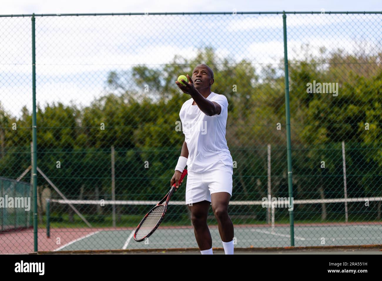 Focused african american male tennis player serving ball on outdoor