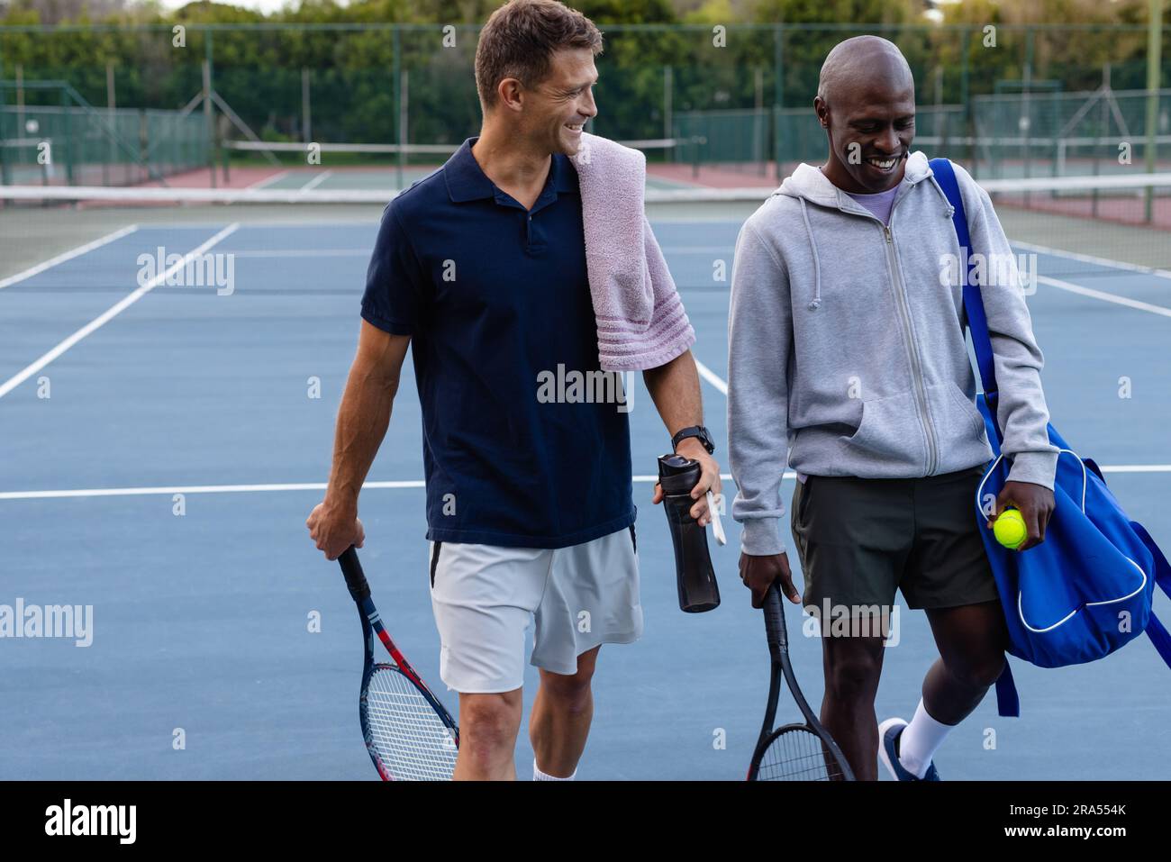 Happy diverse male tennis players with sports bag and rackets talking ...