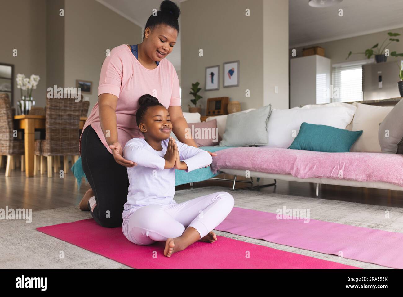 Happy african american mother and daughter doing yoga and meditating in ...