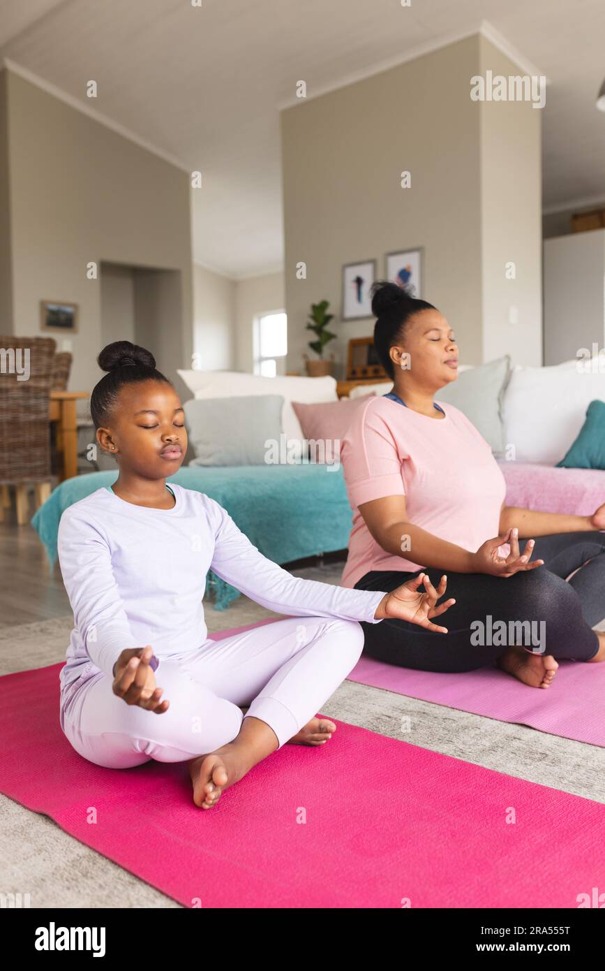 African american mother and daughter doing yoga and meditating in ...