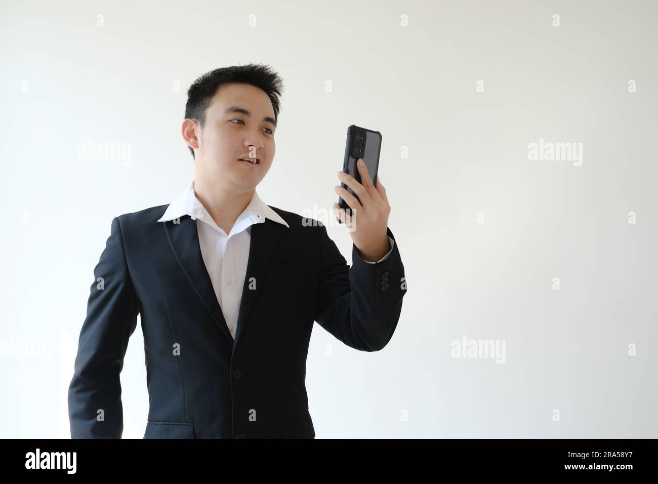 Young Asian business man with unpleasant face expression doing video call on his smartphone. Isolated white background. Suitable for advertisement. Stock Photo