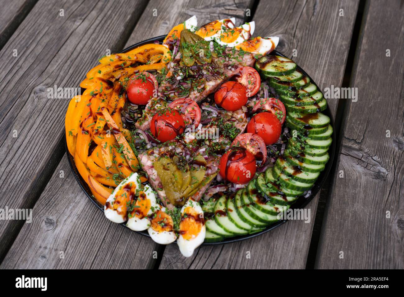 brawn with green cucumber, boiled egg,red onions, cherry tomatoes,yellow paprika, olive oil, balsamic vinegar, chives,  served on a rustic wood table Stock Photo