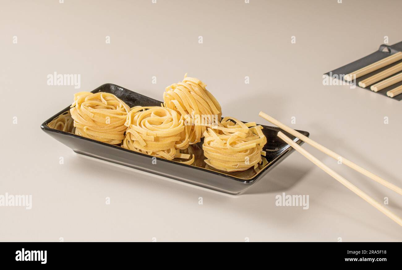 Chinese noodles on a black plate and bamboo chopsticks. Stock Photo