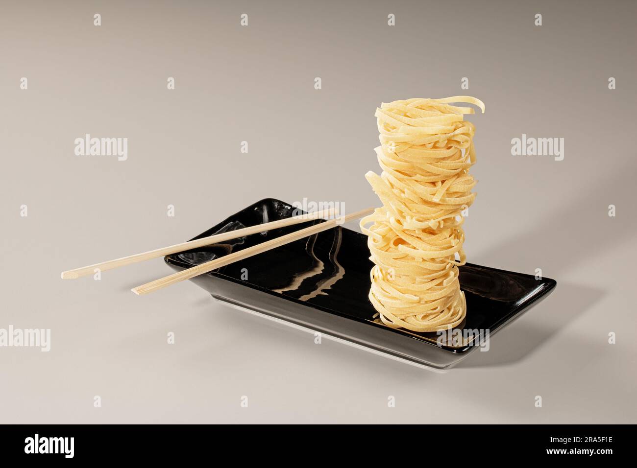 Stack of chinese noodles on black plate and bamboo chopsticks. Stock Photo