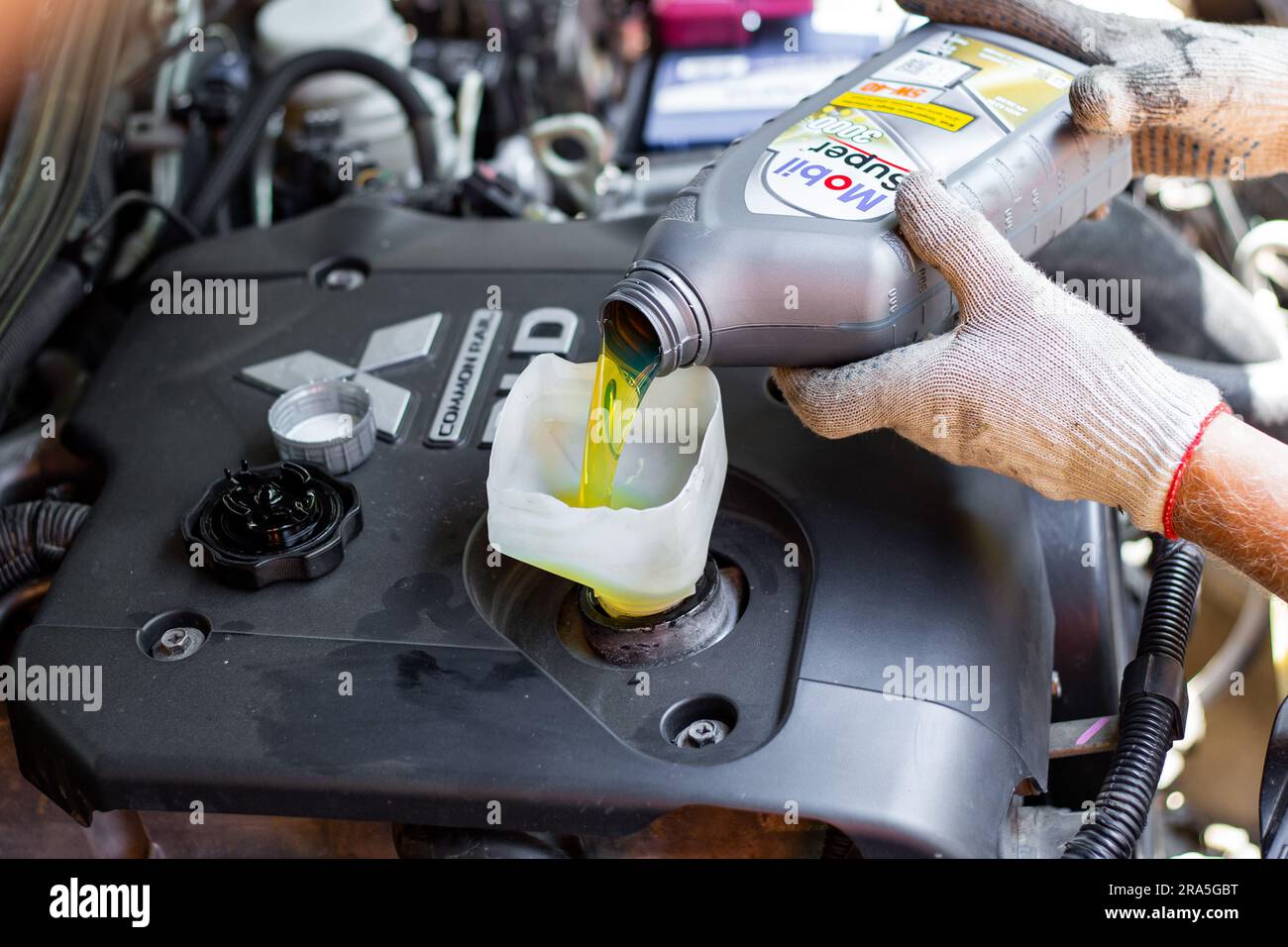 Mitsubishi engine oil change. A car mechanic pours Mobile engine oil