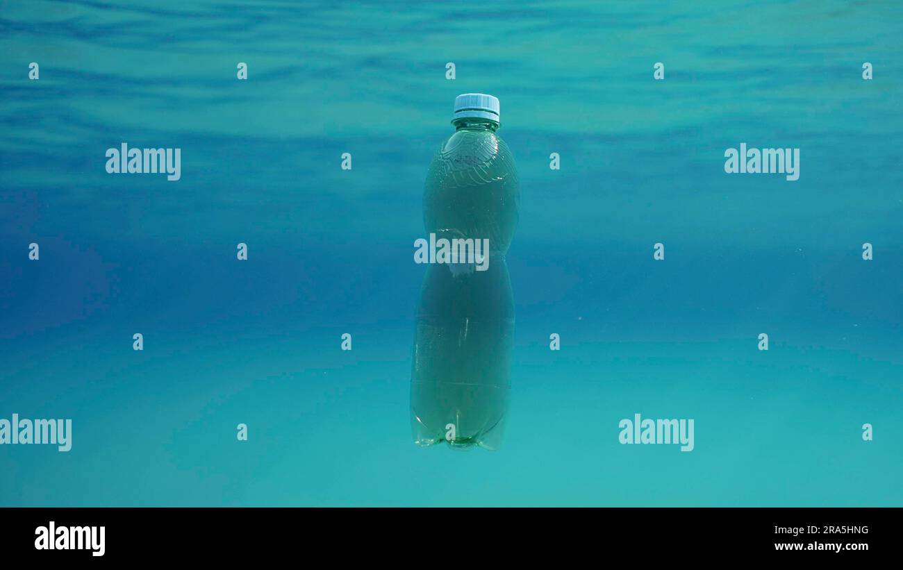 Green plastic bottle drifting under surface of blue water. Plastic pollution of Ocean, Discarded plastic bottle floats underwater in sunlight, Red Stock Photo