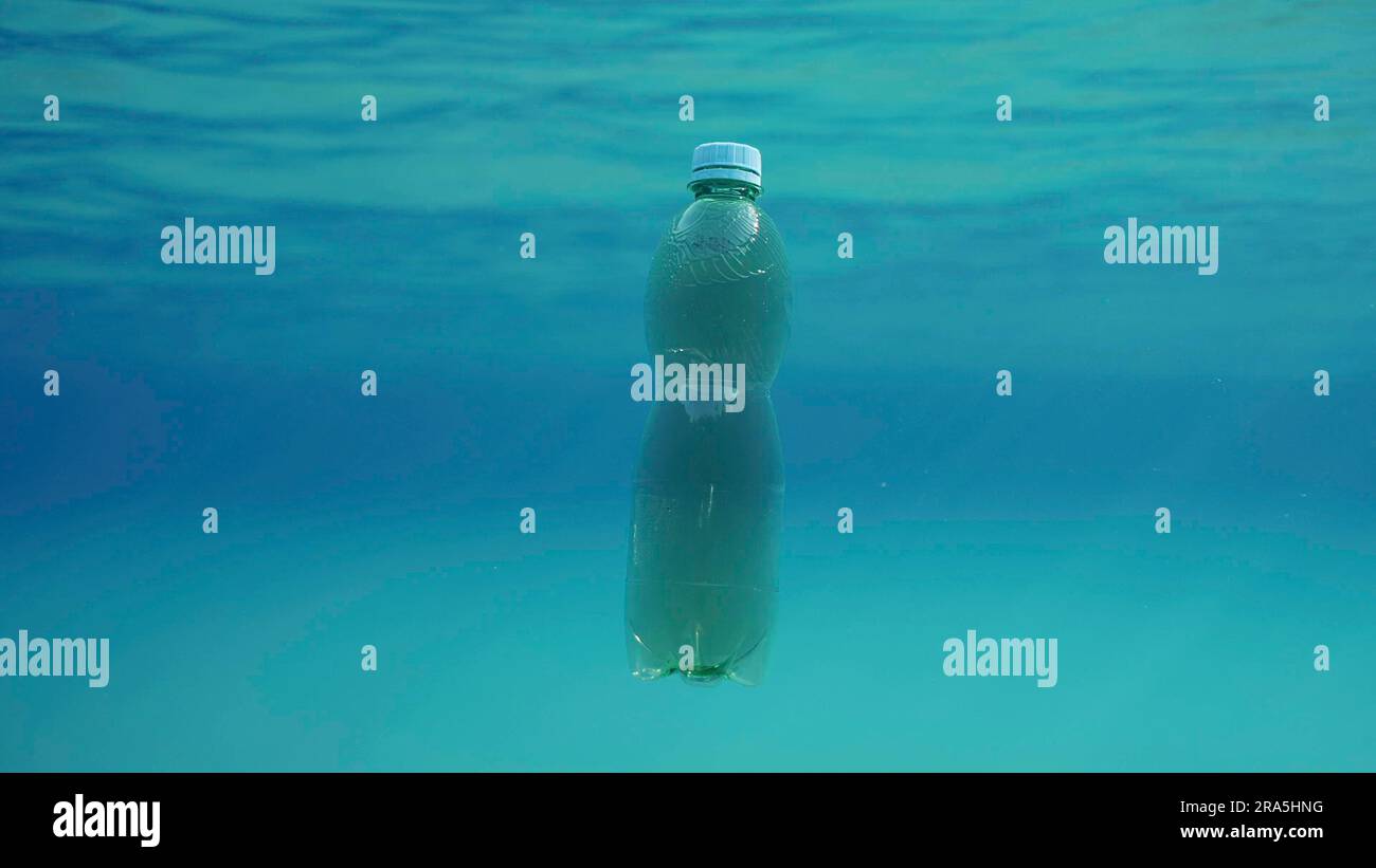 Green plastic bottle drifting under surface of blue water. Plastic