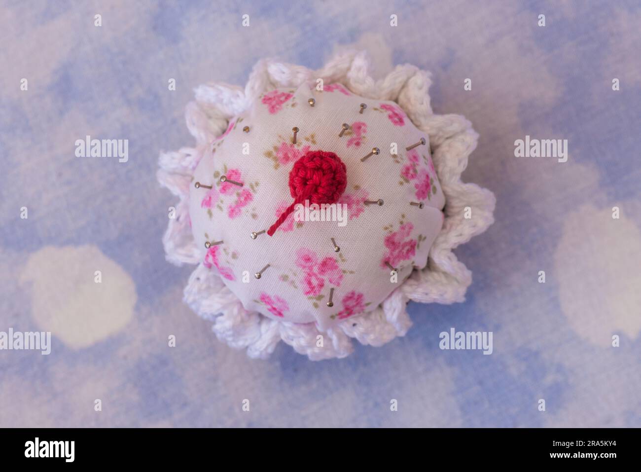 details of a cupcake-shaped pincushion, on a texturede background Stock Photo