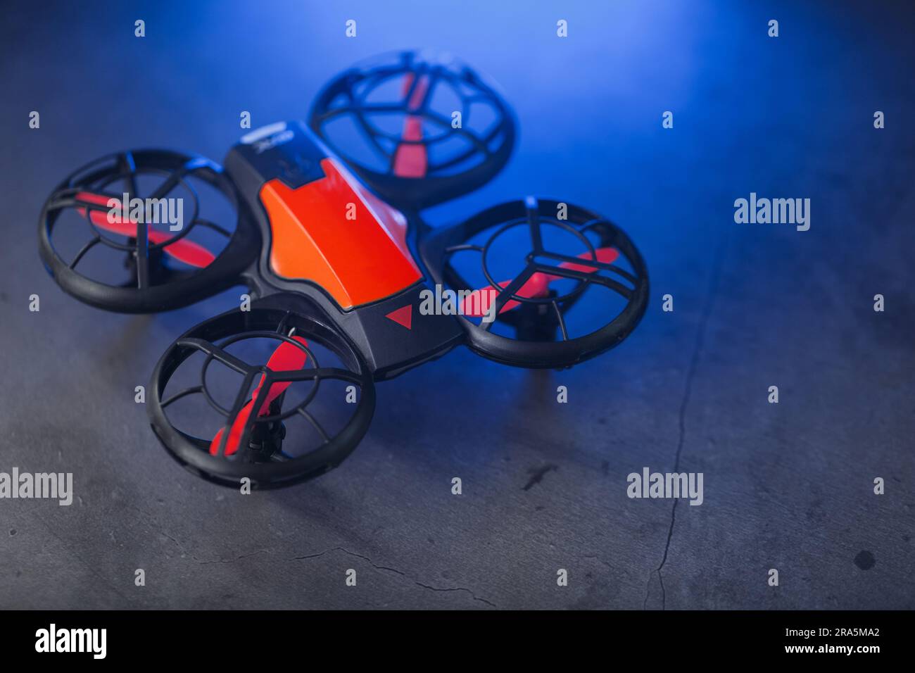 Orange quadcopter mini spy drone on a dark background with blue backlight and free space Stock Photo