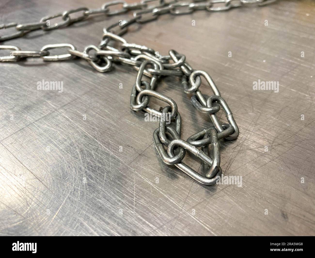 A large iron metal strong powerful shiny chain with links lies on an iron industrial table. Hand-held locksmith tools. The background. Stock Photo