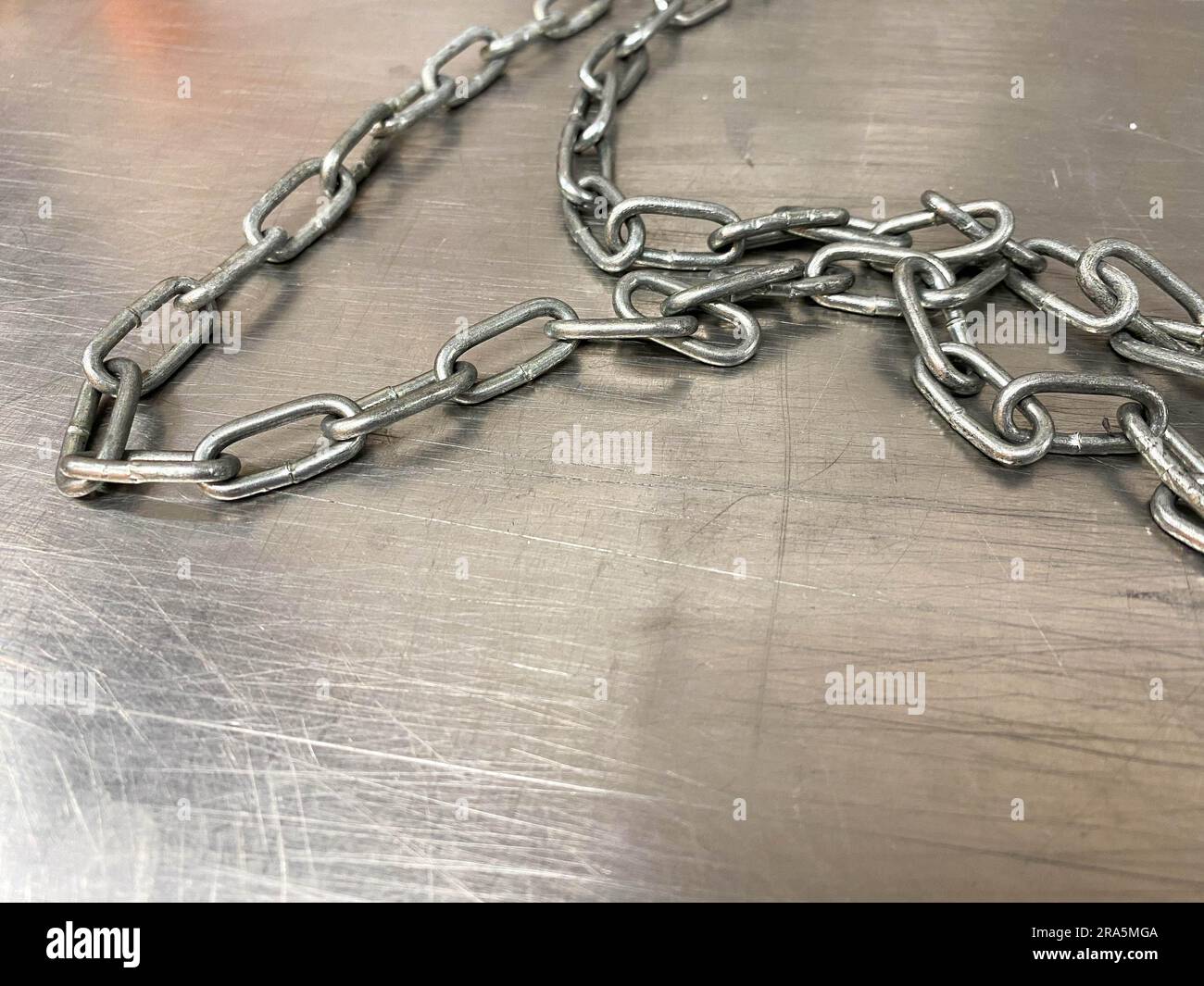 A large iron metal strong powerful shiny chain with links lies on an iron industrial table. Hand-held locksmith tools. The background. Stock Photo