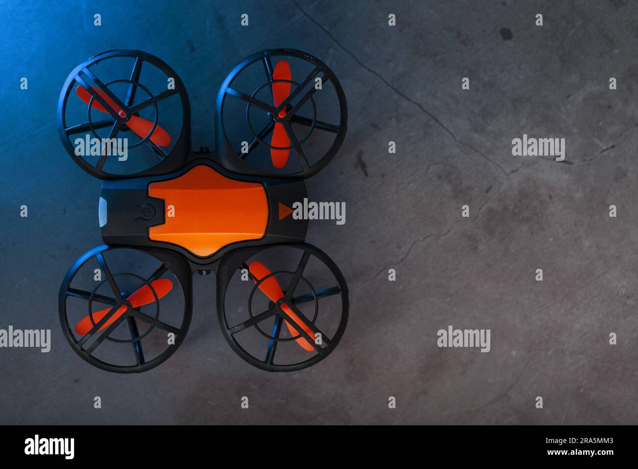 Orange quadcopter mini spy drone on a dark background with blue backlight and free space Stock Photo