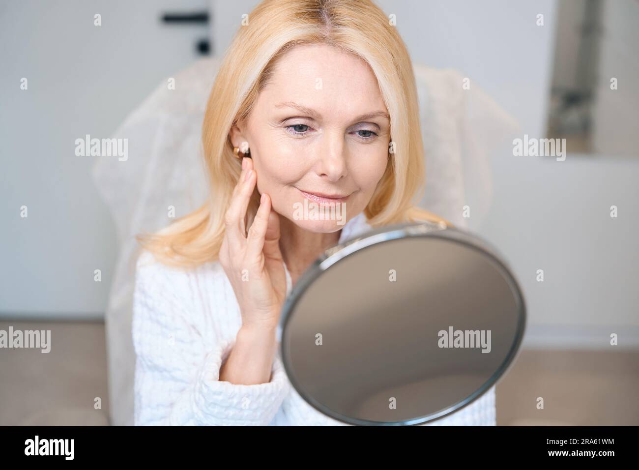 Happy mature lady looking in mirror at cosmetologist office Stock Photo