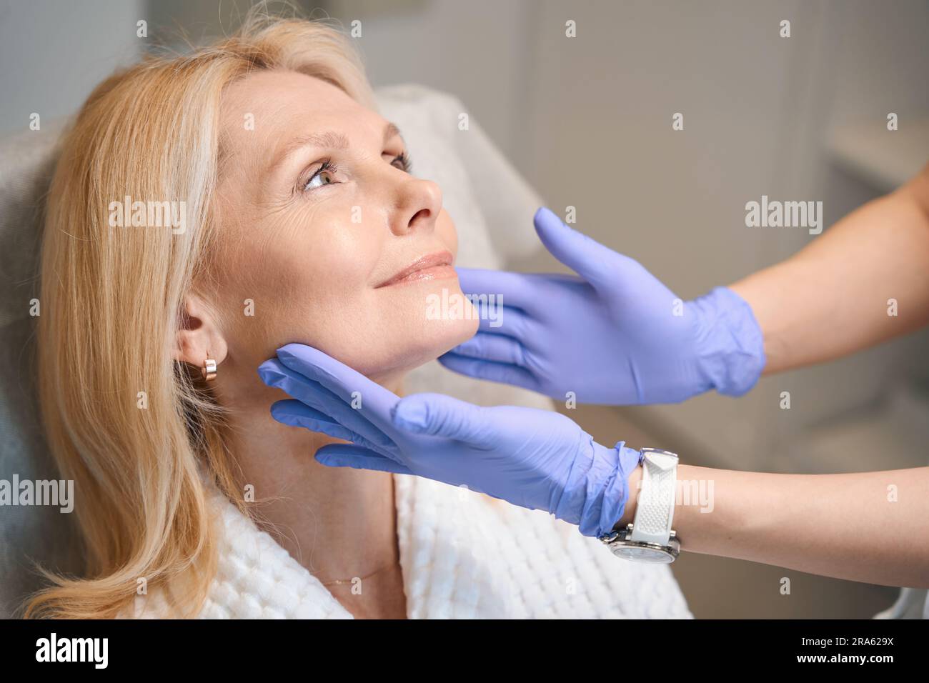 Hands in medical gloves touching happy woman face Stock Photo