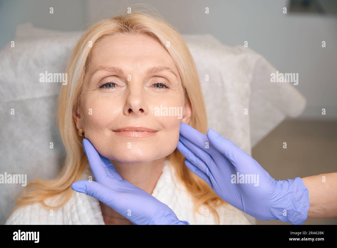 Hands in medical gloves touching happy woman face Stock Photo