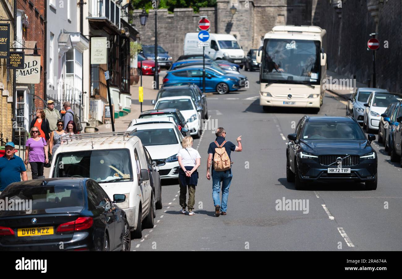 People, probably tourists, walking along a busy road despite there being cars, in a British town in England, UK. Stock Photo