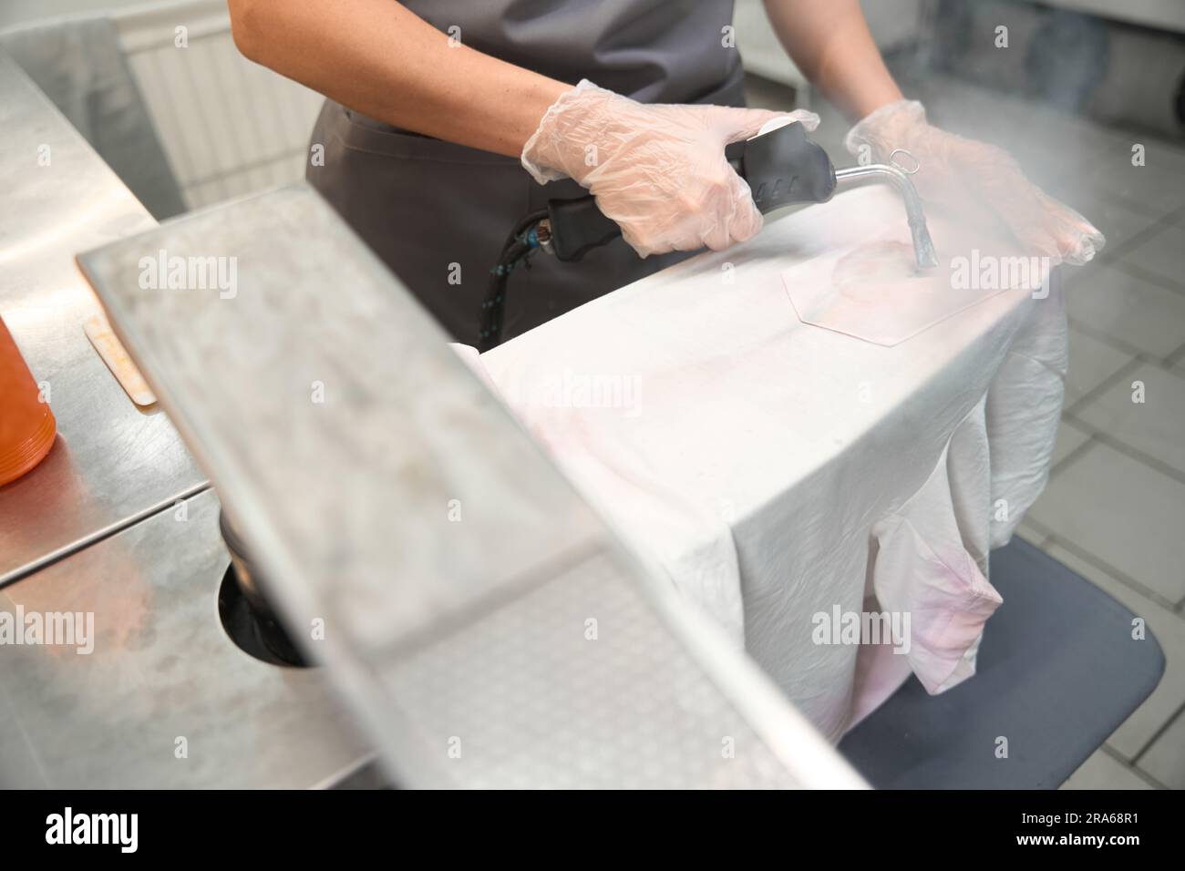 Skilled drycleaner using steam gun to remove stain from tshirt Stock